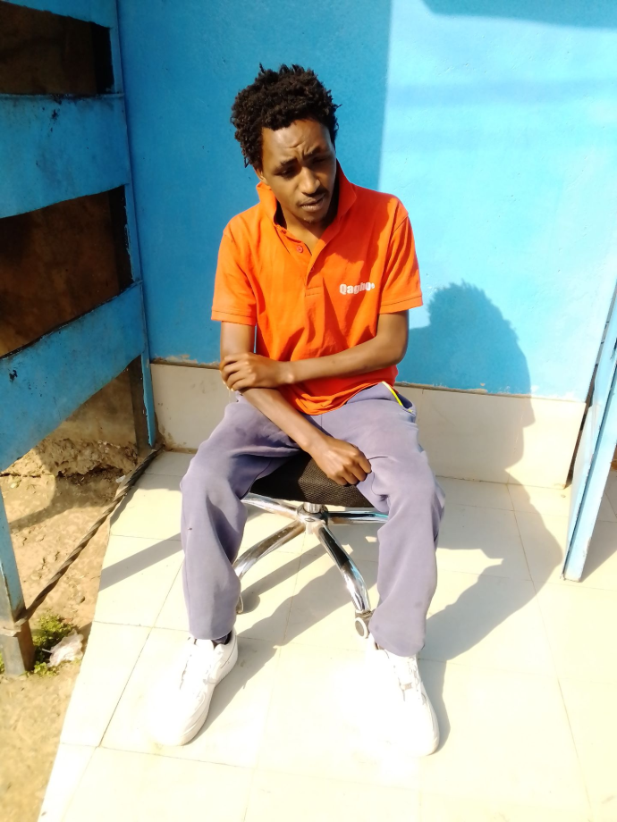 A solitary portrait of Imanueli Daudi, the Successor, seated in a controlled sanctuary environment, looking downward in deep contemplation against a blue background, exemplifying internal discipline and focus.
