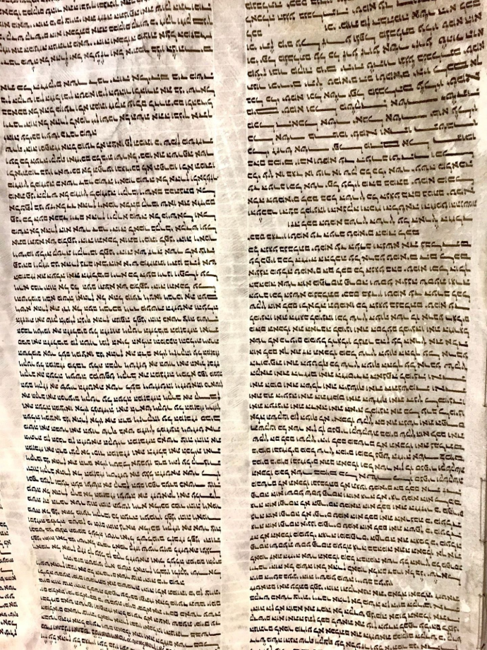 A close-up photograph of an authentic ancient Hebrew manuscript scroll fragment showing handwritten biblical text from the Old Testament Book of Isaiah, found near the Dead Sea.